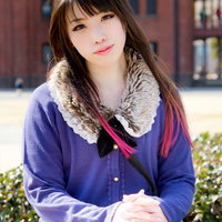 赤レンガの壁を背に足を組んで立つ女性の写真