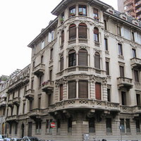 ミラノの街角に立つクリーム色の歴史的建造物と路上駐車風景の写真