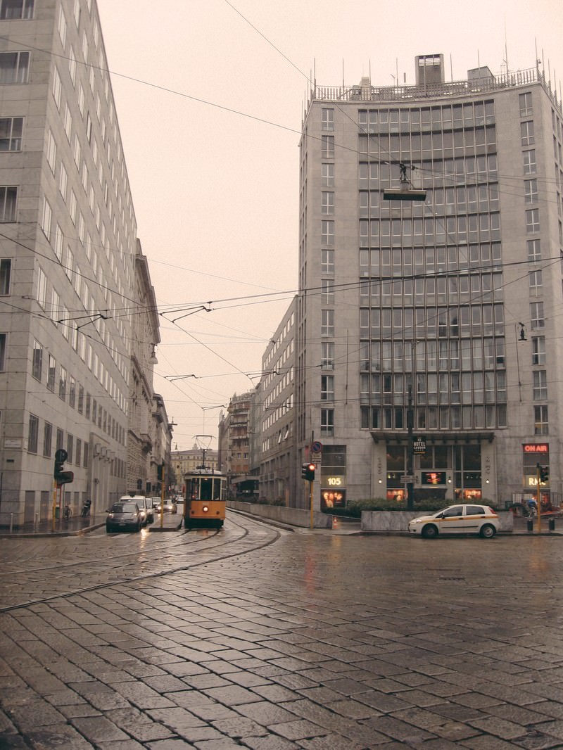 雨のミラノで石畳の交差点を曲がる黄色い路面電車