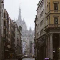 ミラノの大聖堂へと続く路地で傘を差す通行人、雨のヨーロッパの街並みの写真