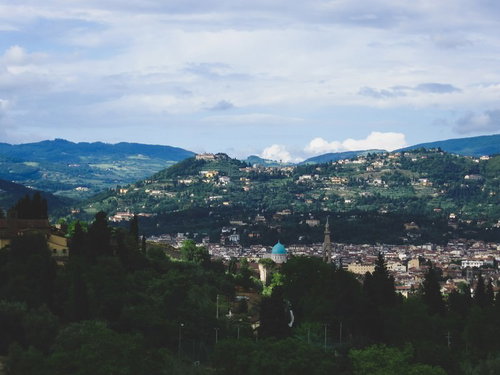 緑の丘陵に囲まれたフィレンツェの歴史的な街並みと赤い屋根の建物