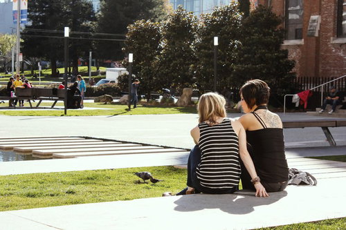 芝生の広場に座る二人の後ろ姿と海外の大学