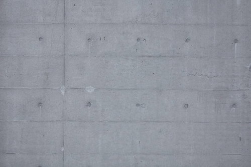 丸い穴やくぼみと縦横の継ぎ目が見えるコンクリート壁のテクスチャー