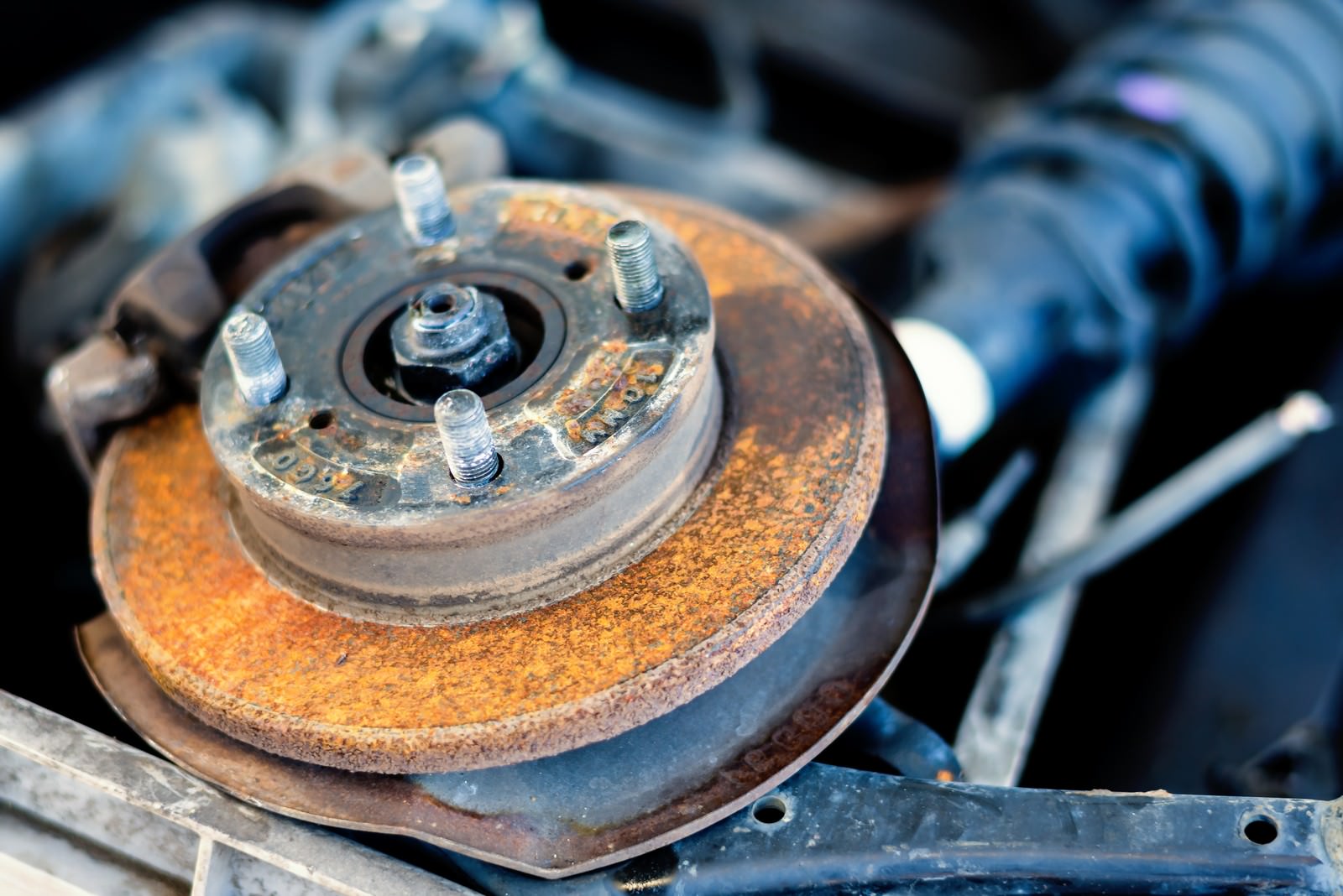 錆びたブレーキディスクにボルトが付いており、背景に解体機械が見える