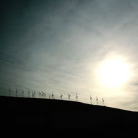 夕暮れの丘に並ぶ風力発電の風車の写真