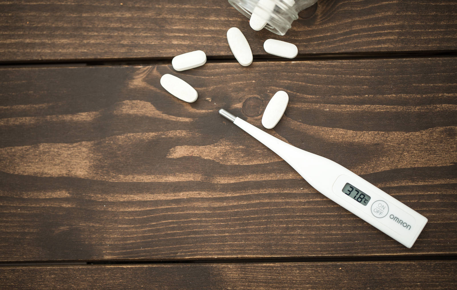 木製テーブルの上の体温計と白い錠剤