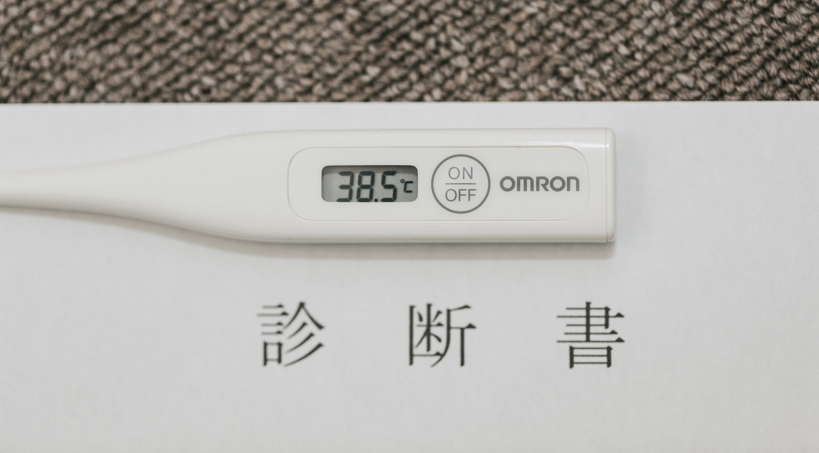 白い診断書の用紙の上に置かれた白いデジタル体温計。液晶画面に38.5℃と表示されている