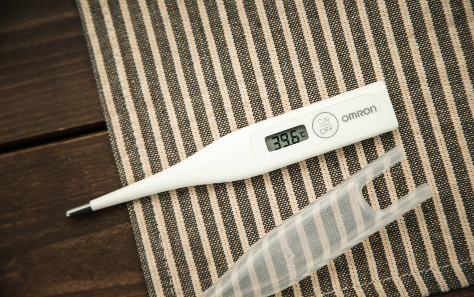 Omron electronic thermometer placed on white sheets, displaying 39.6°C