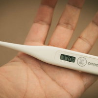 手のひらに乗せた体温計が37.0℃（微熱）を表示の写真
