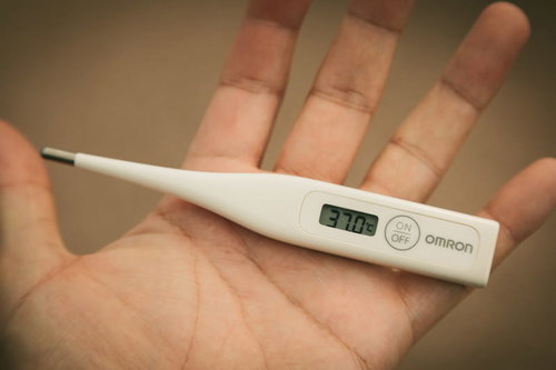 手のひらに乗せた体温計が37.0℃（微熱）を表示