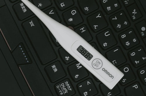 進捗ダメです。黒いキーボードの上に置かれた白い体温計