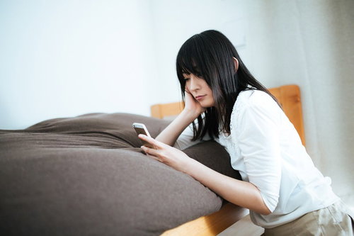 既読スルーにショックを受ける失恋女子がソファーでスマホを見つめる