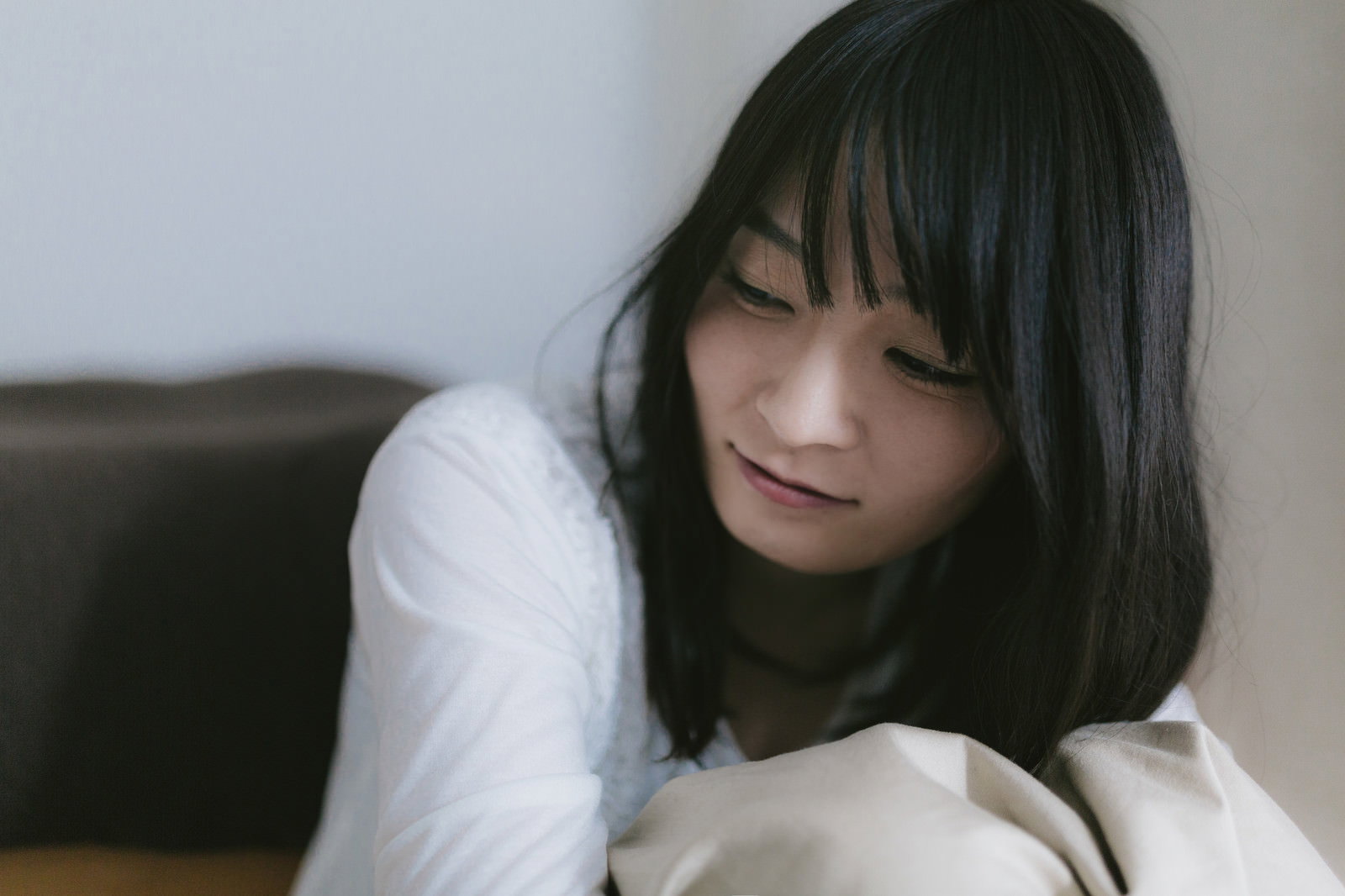 白いシャツを着てソファーに座り下を向いて思い詰める女性［モデル：たけべともこ］