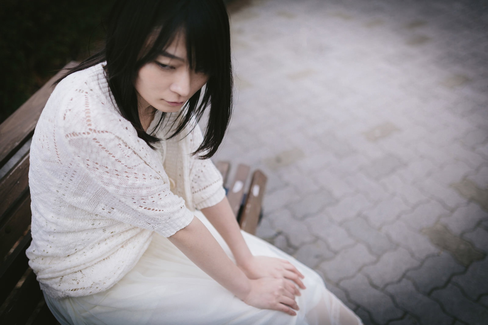 ベンチに座り横を見つめる白いニットの女性［モデル：たけべともこ］