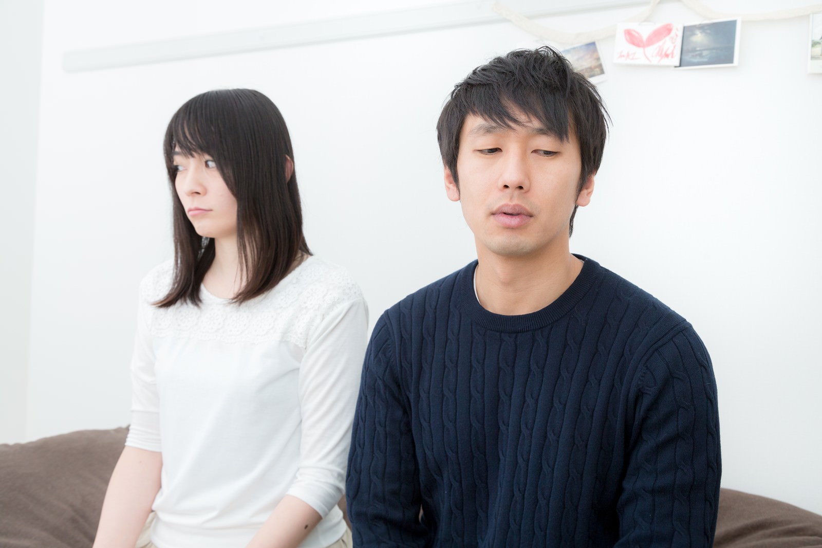 ソファで無言のまま視線を落とすカップル［モデル：大川竜弥 たけべともこ］
