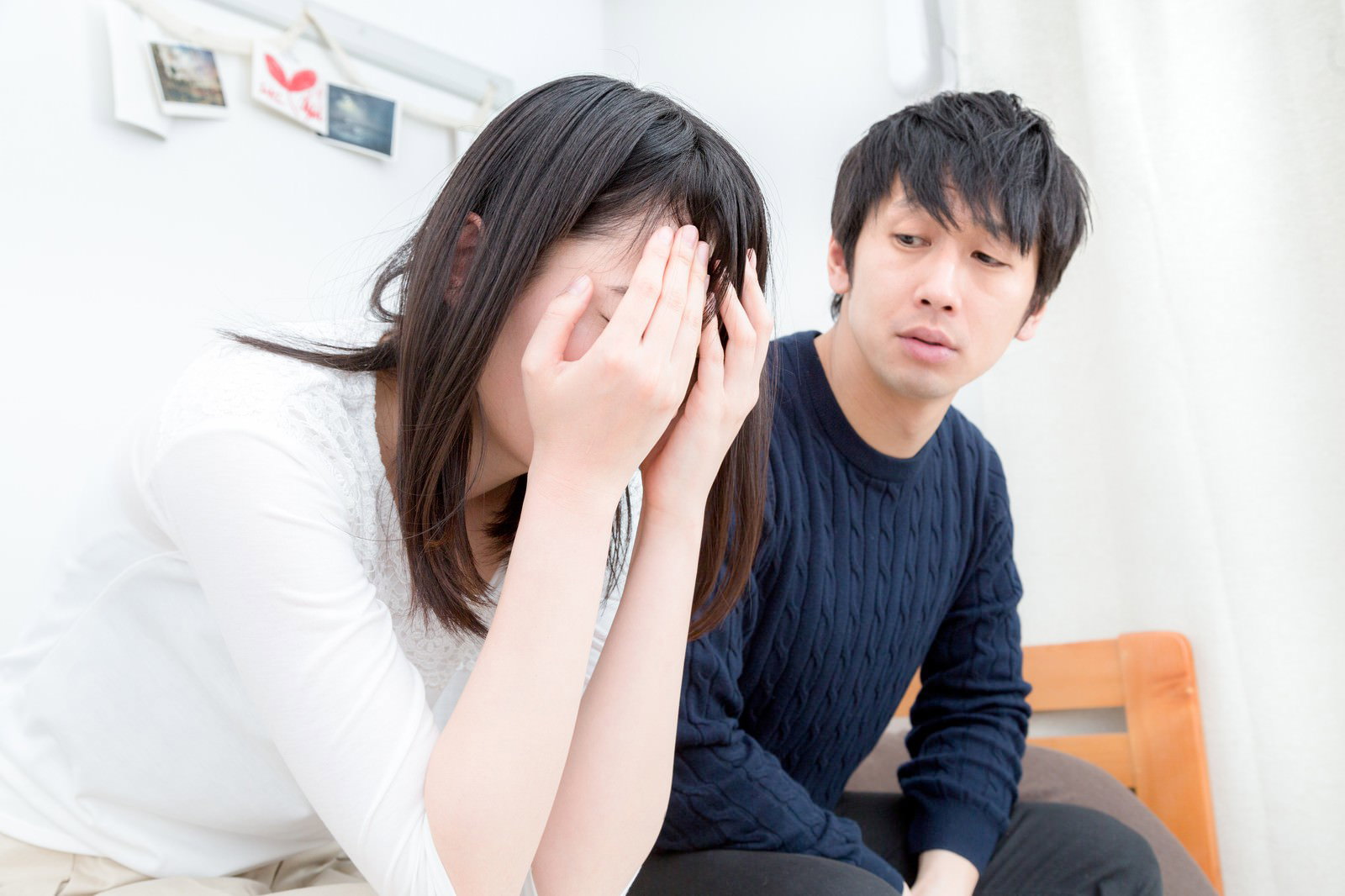 室内で両手で顔を覆いながら泣く女性と、冷徹な表情で下を向く男性が座っている［モデル：大川竜弥 たけべともこ］