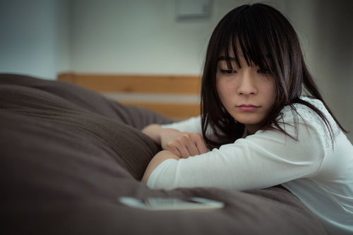 彼からの返事をじっと待つ女性とスマホ、ベッドでの不安な表情