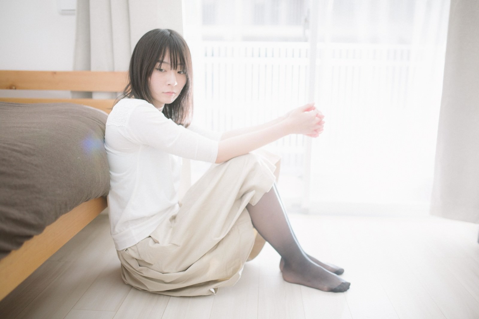 ベッドに座り下を向く女性［モデル：たけべともこ］