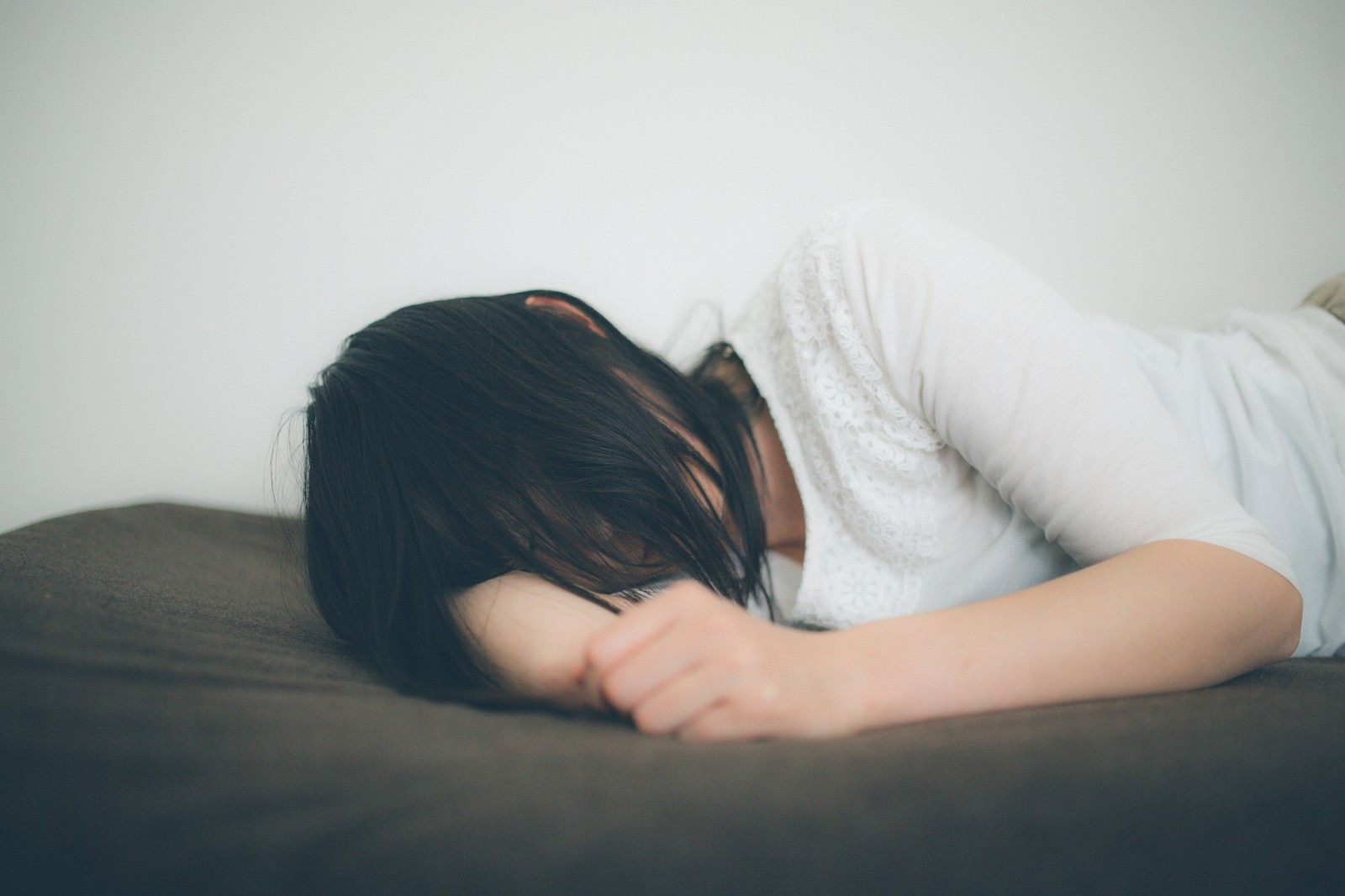 ベッドで腕枕をして横たわる失恋女子の後ろ姿［モデル：たけべともこ］