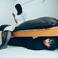 ベッドの下に隠れる男とスマホを見つめる女性の写真
