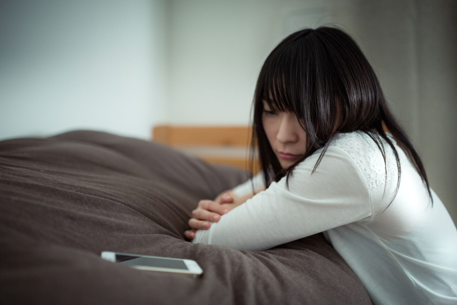 ソファーに座ってスマートフォンを見つめながら俯く女性［モデル：たけべともこ］