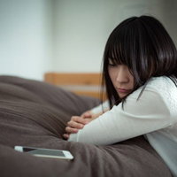 元カレからの着信を待つ失恋女子がソファーで下を向くの写真