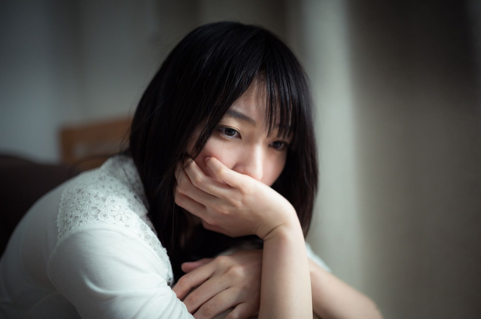 頭を手で押さえながら下を向く落ち込んだ女性［モデル：たけべともこ］