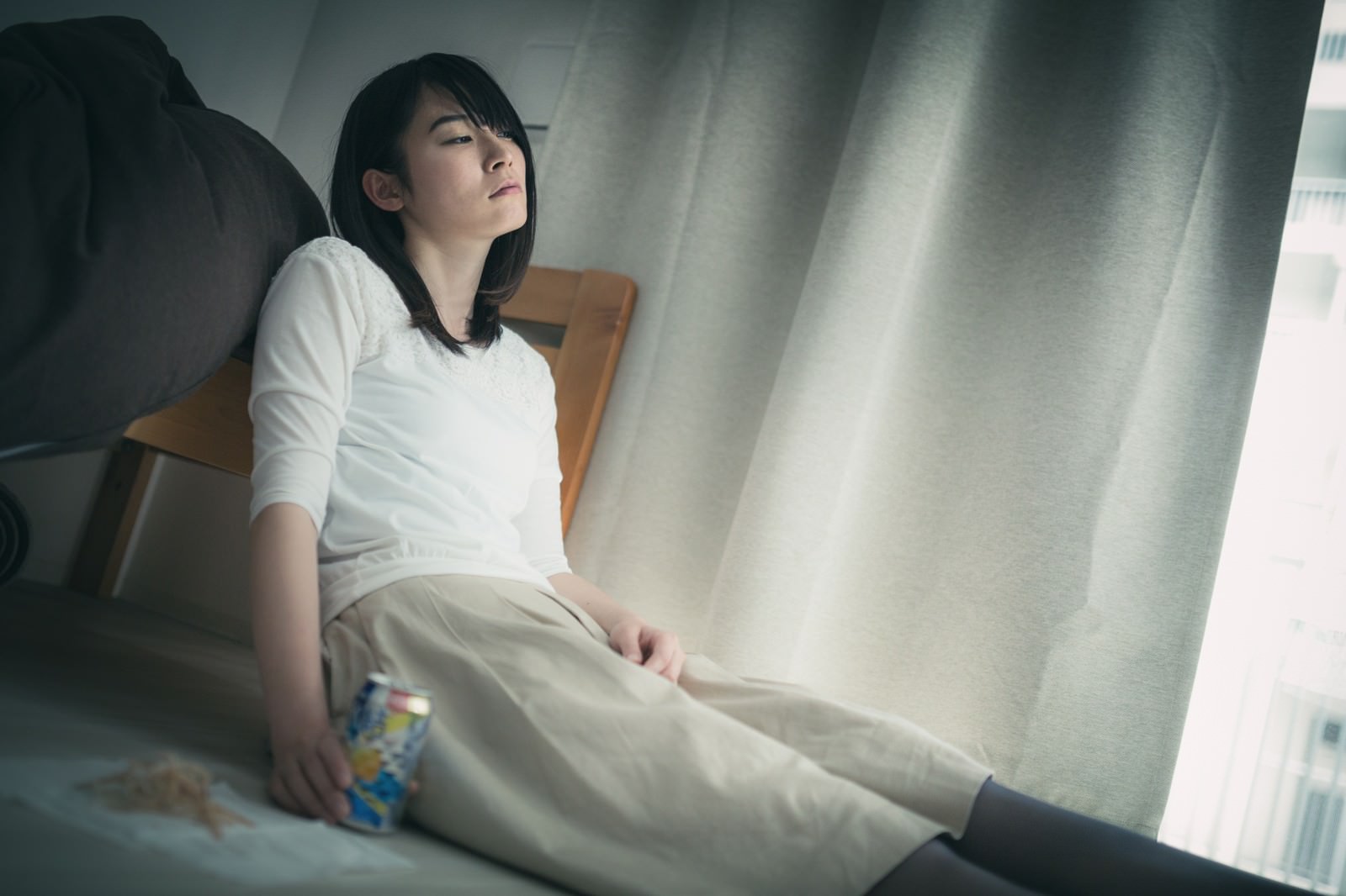 窓辺に座り缶チューハイとエイヒレを前にする女性［モデル：たけべともこ］