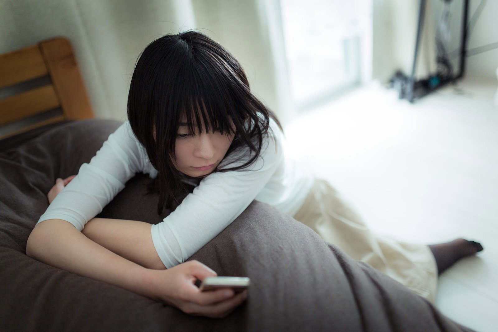 ソファーに座ってスマートフォンを見つめる黒髪の女性［モデル：たけべともこ］