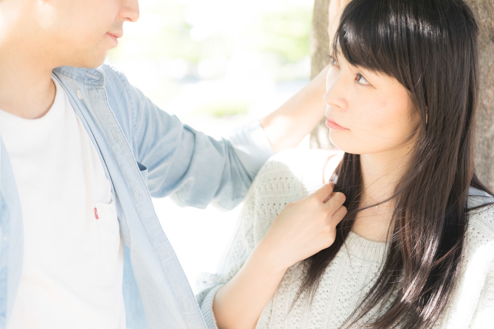 白い壁の前で壁ドンする男性と見つめ合う黒髪の女性［モデル：たけべともこ］