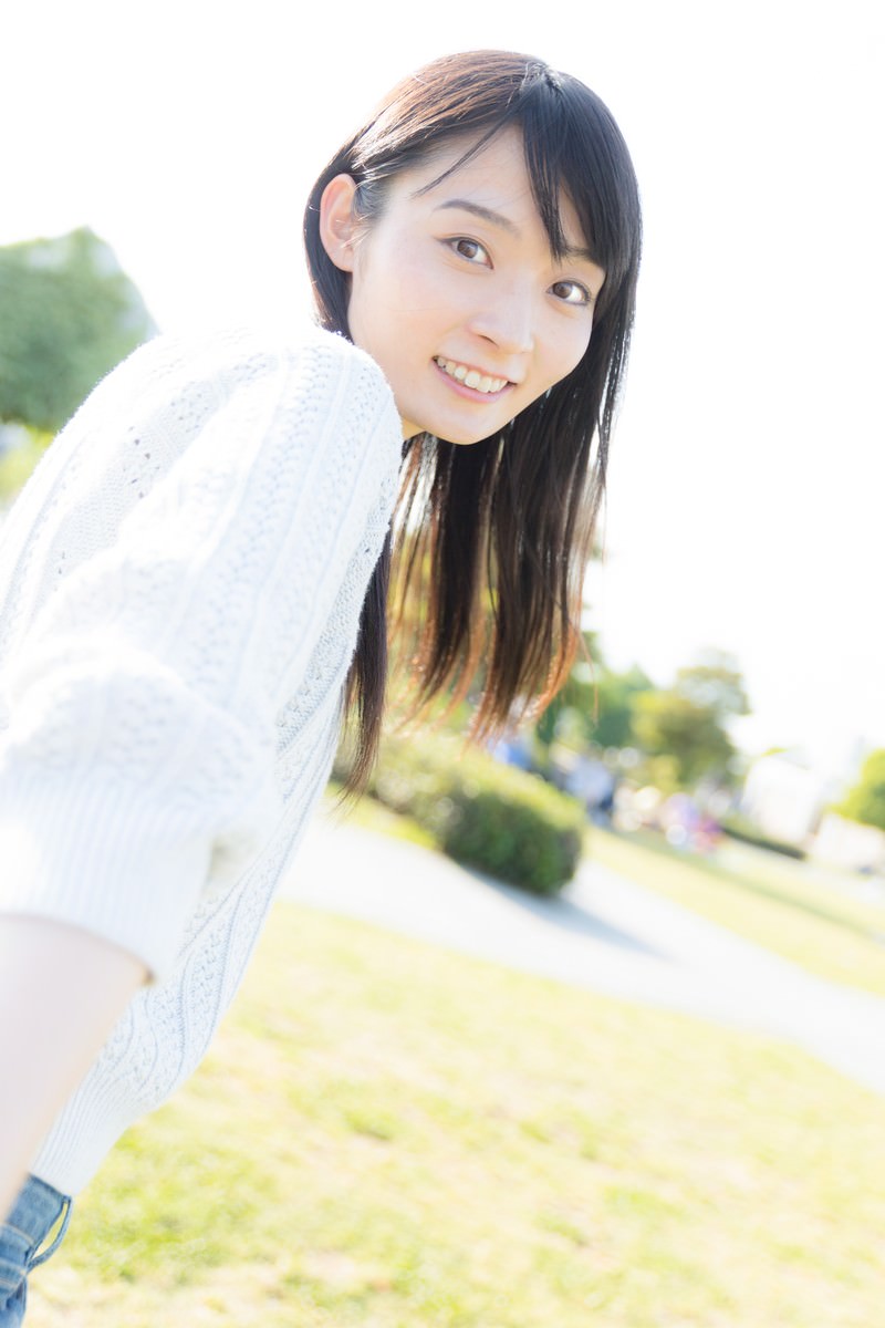 白いワンピースを着たロングヘアの女性が公園で優しく微笑んでいる［モデル：たけべともこ］