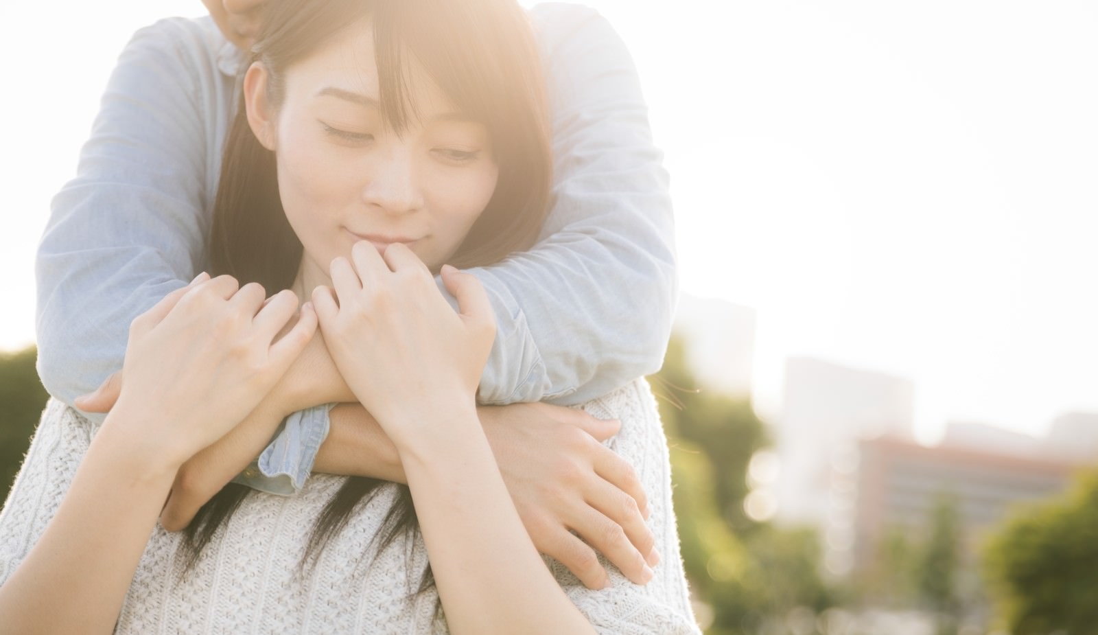 後ろから男性に抱きしめられて幸せそうな表情を見せる女性［モデル：たけべともこ］
