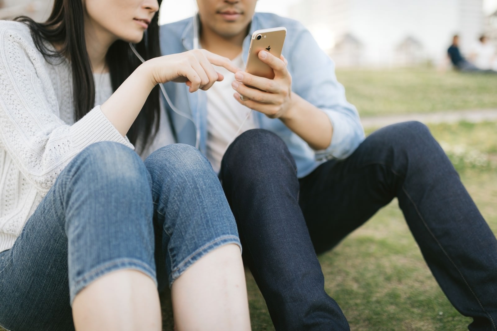 イヤホンを共有してスマートフォンで音楽を聴く恋人［モデル：たけべともこ］