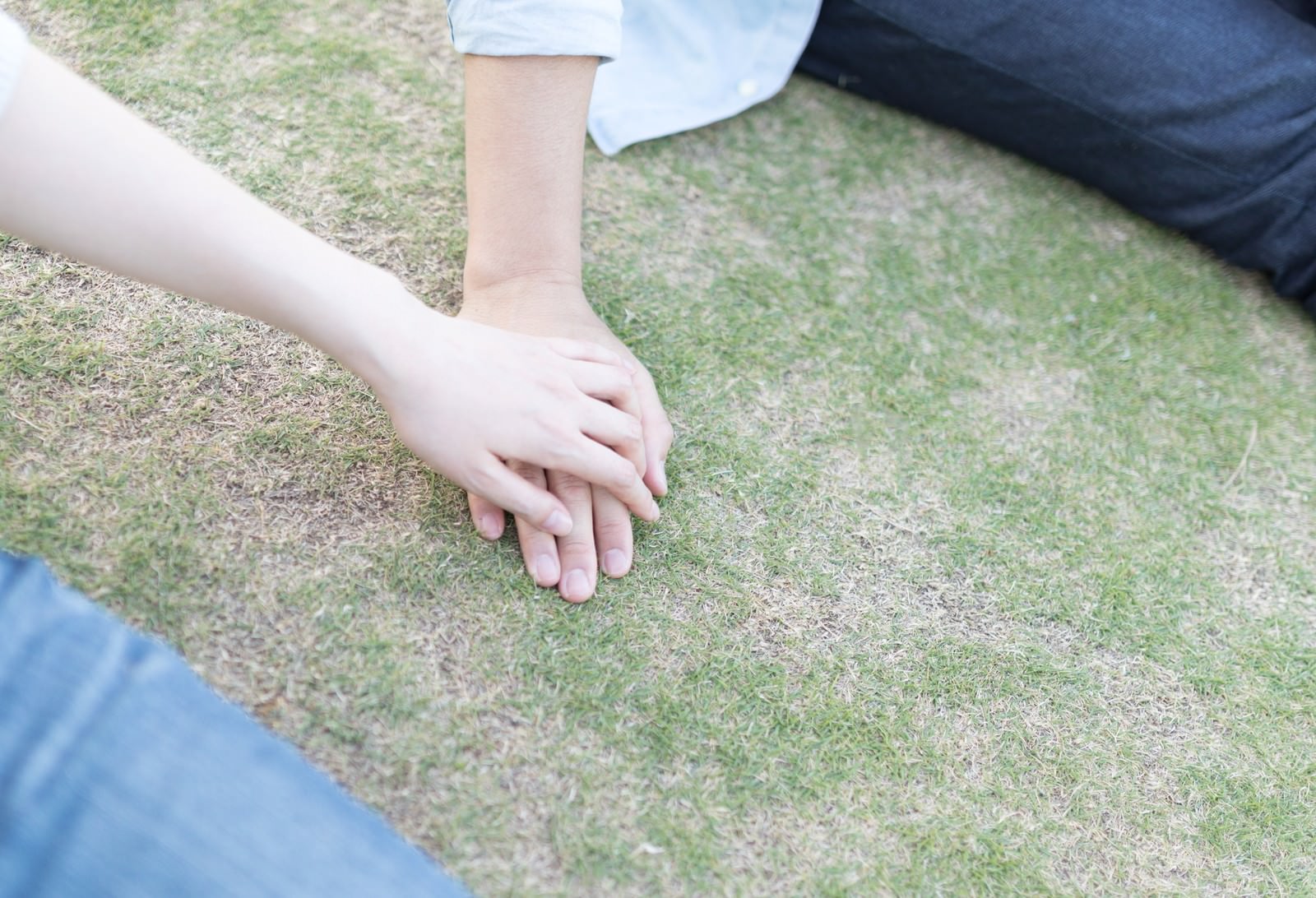 芝生の上で彼の手に手を重ねる女性の手元