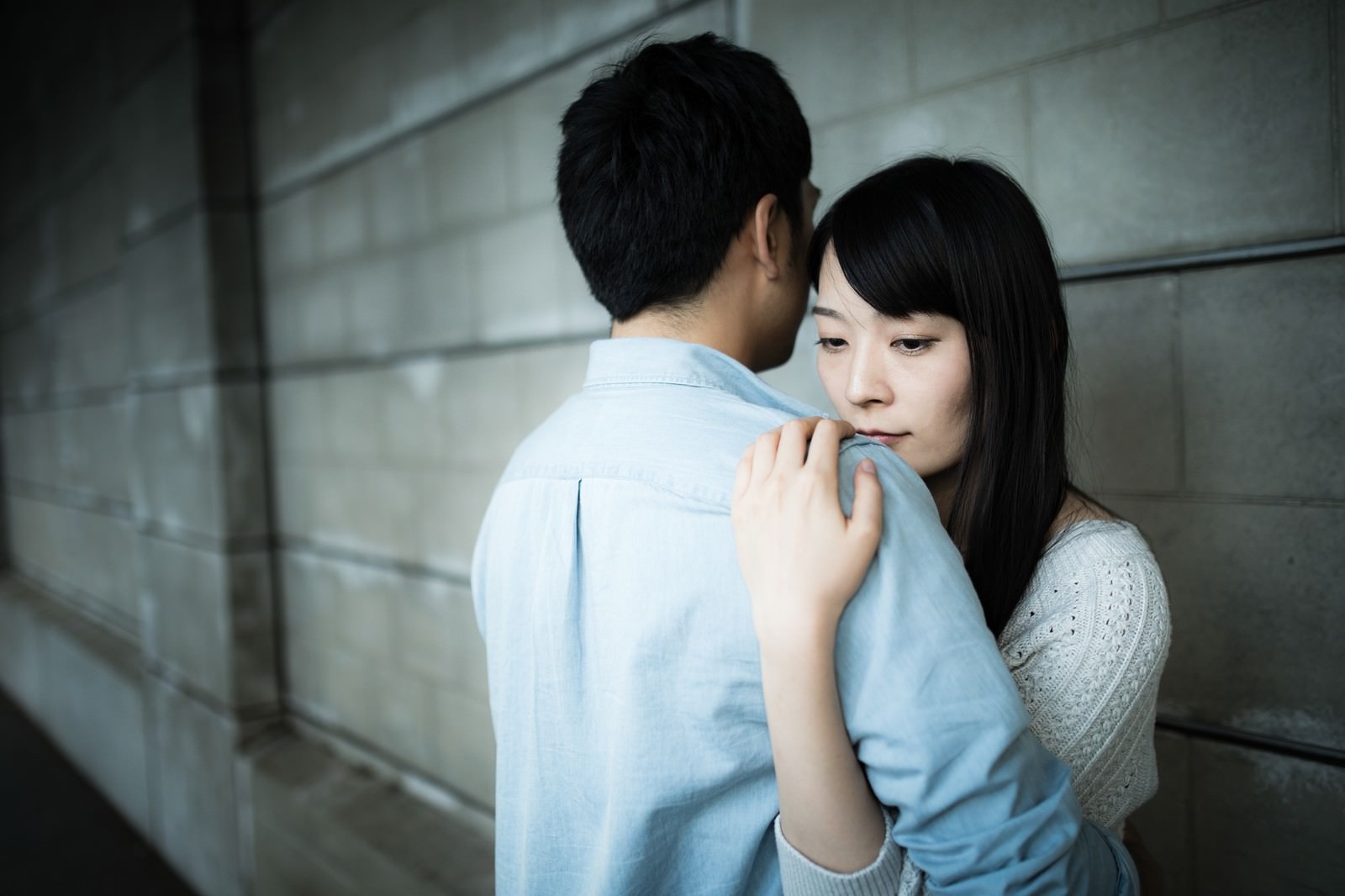 コンクリート壁の前で男性が女性を抱きしめているカップル［モデル：たけべともこ］