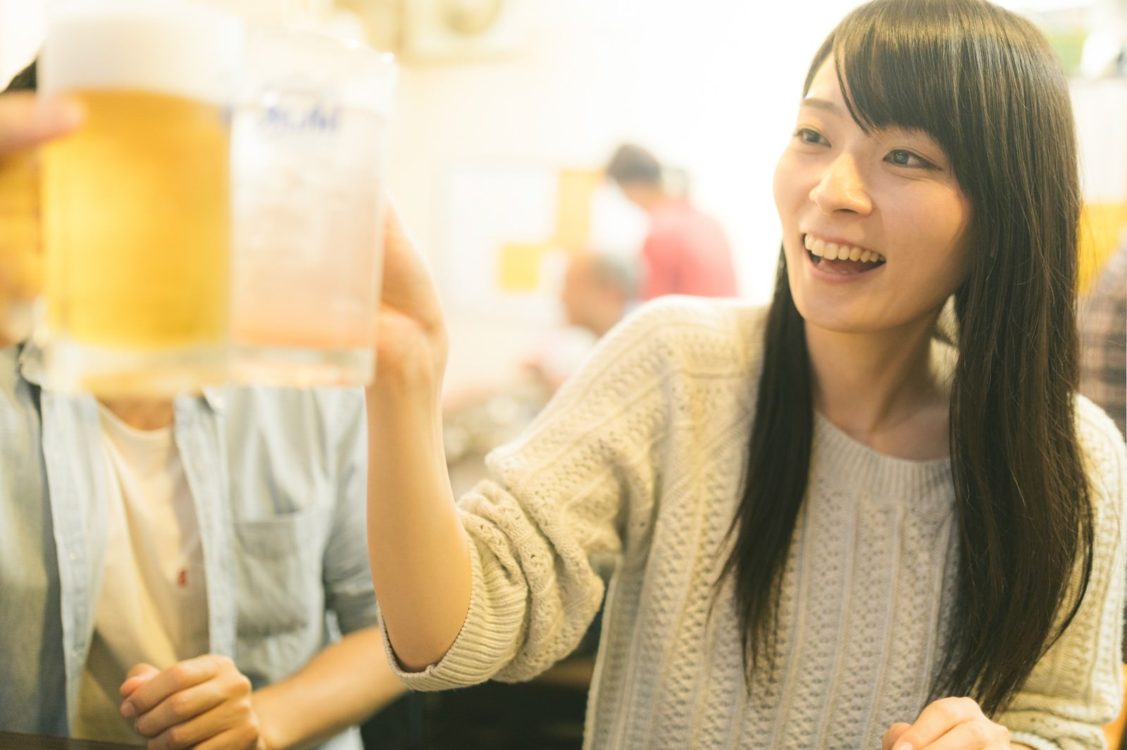 居酒屋でビールジョッキを持って笑顔で乾杯する女性［モデル：たけべともこ］