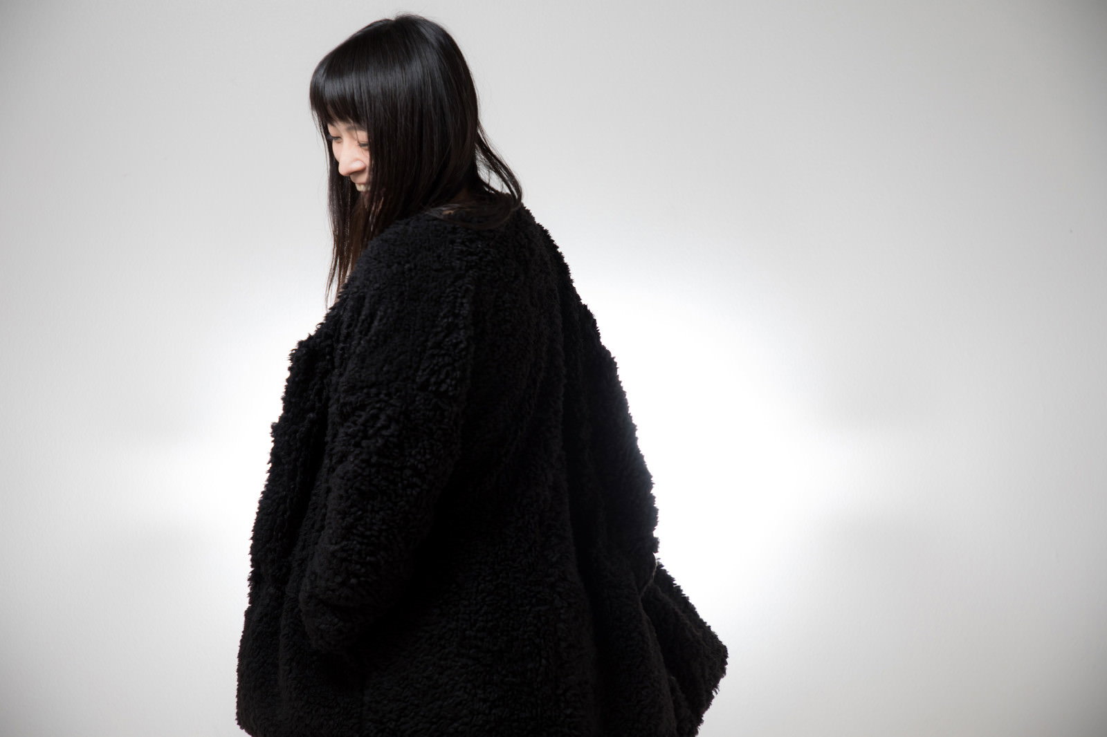 黒いもこもこの上着を着て横向きに立つ女性
