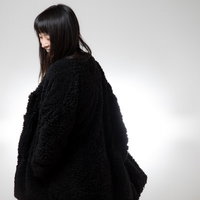 ロン毛じゃないよ、上着だよ。黒いもこもこ素材の羽織りを着た女性の写真