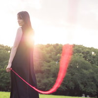 私たちは赤い糸で結ばれているの（ウフフ）緑の丘陵を背に立つ女性の写真