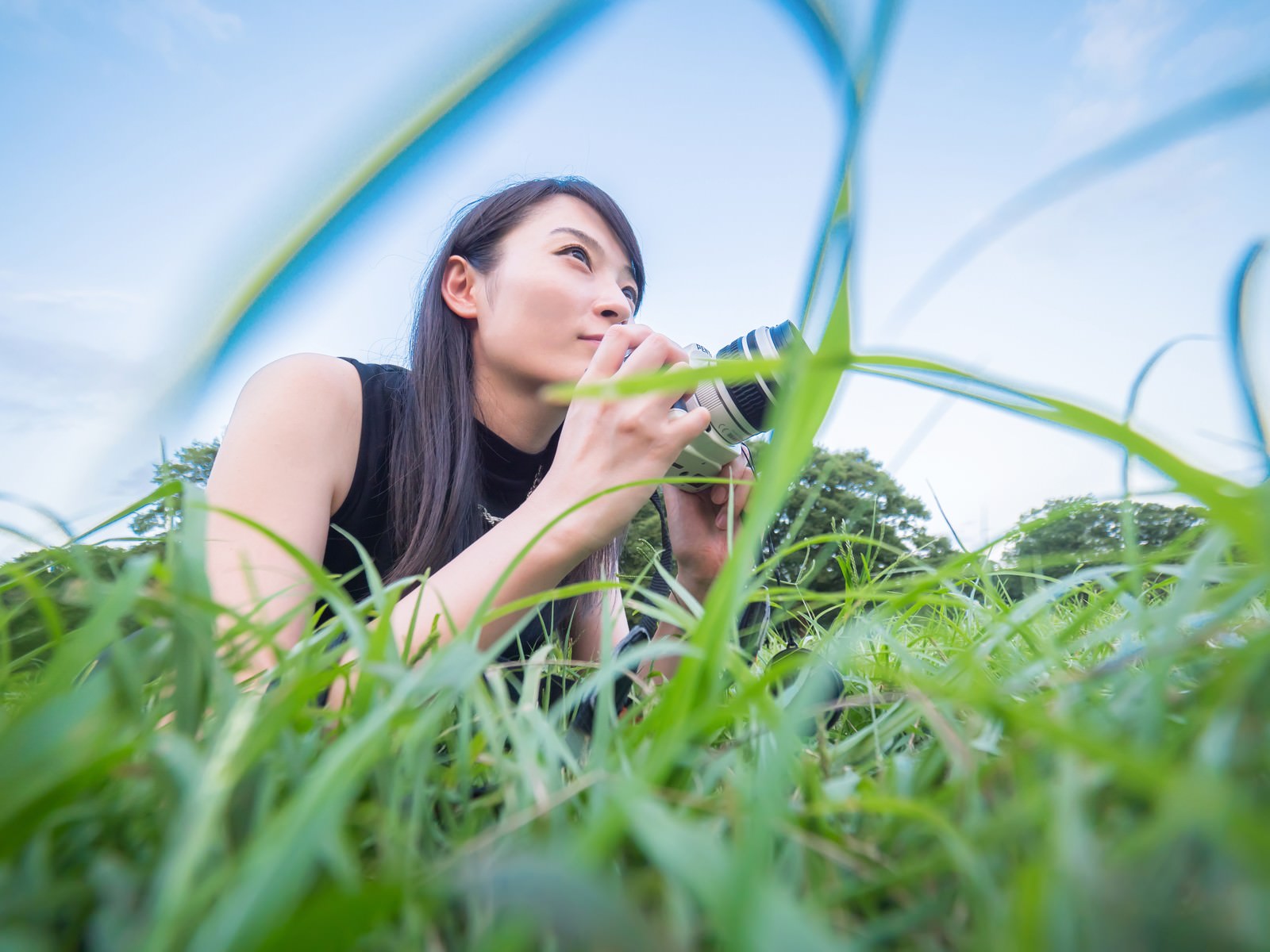 草むらで低い位置からカメラを構える女性フォトグラファー［モデル：たけべともこ］