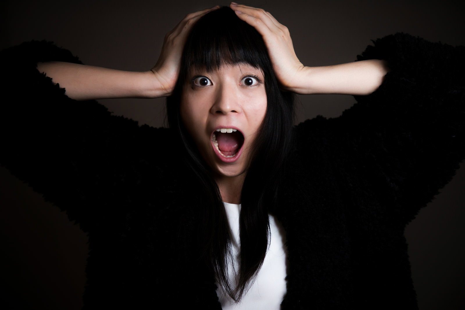 両手を頭に当てて口を開けて叫ぶ黒髪の女性のアップショット［モデル：たけべともこ］