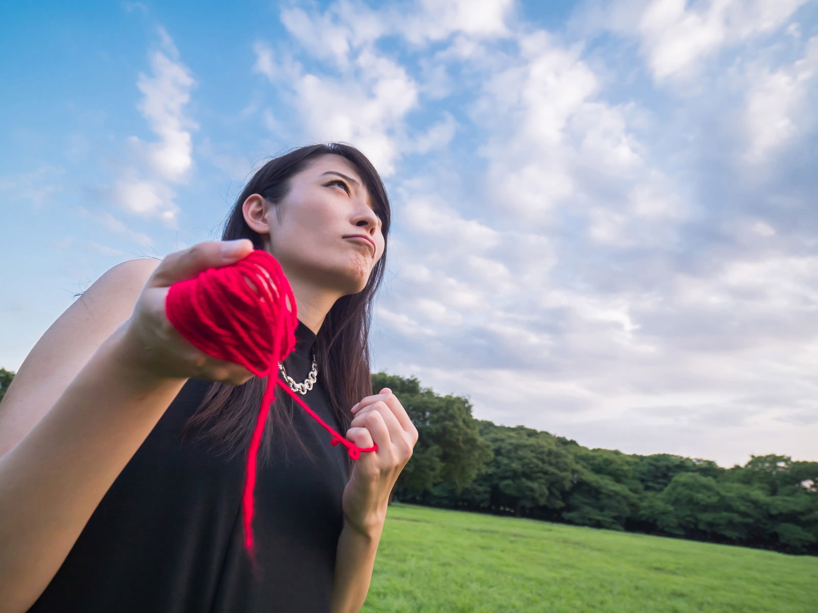 赤い糸を握りしめ青空を見上げる女性［モデル：たけべともこ］