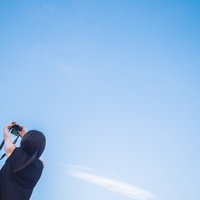 青空の下でコンパクトカメラをかざして自撮りする女性の写真