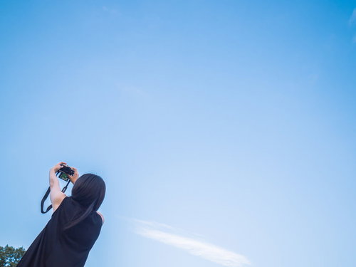 青空の下でコンパクトカメラをかざして自撮りする女性