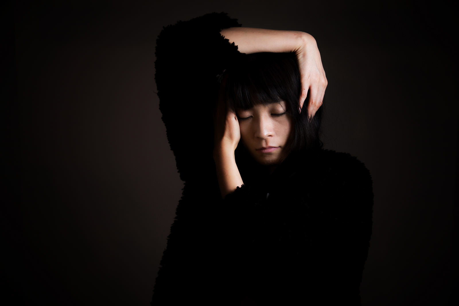 頭を両手で抱えてうつむく黒服の女性［モデル：たけべともこ］