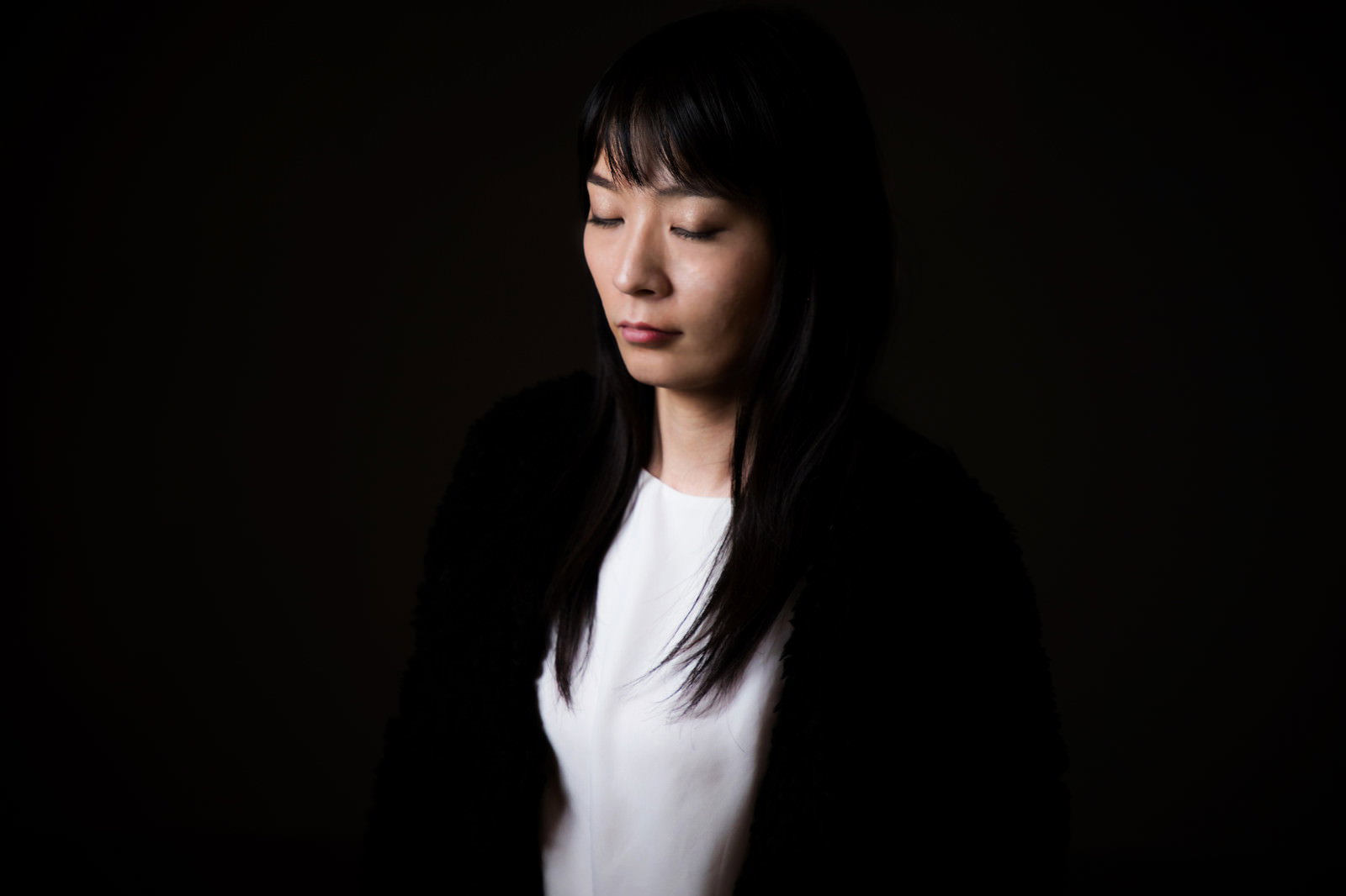 目を閉じて静かに立つ黒髪の女性［モデル：たけべともこ］