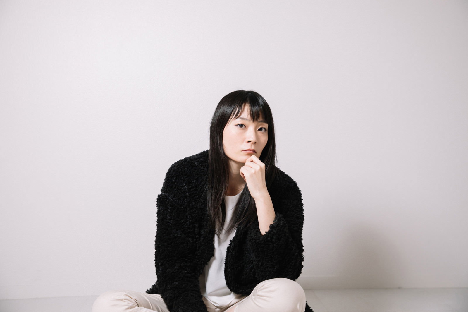 黒いカーディガンで頬に手を当てて上を見つめる女性［モデル：たけべともこ］