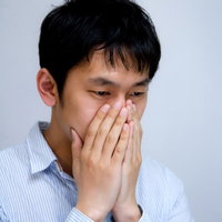 白い背景の前で口元に手をやり青ざめた表情の男性の写真