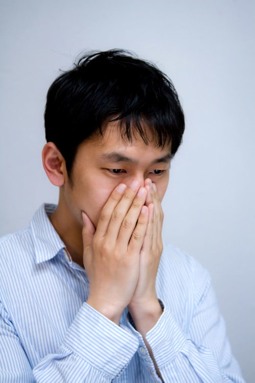 白い背景の前で口元に手をやり青ざめた表情の男性