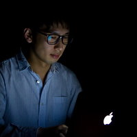 暗いオフィスでPCの光だけに照らされるブラック企業で残業する男性の写真